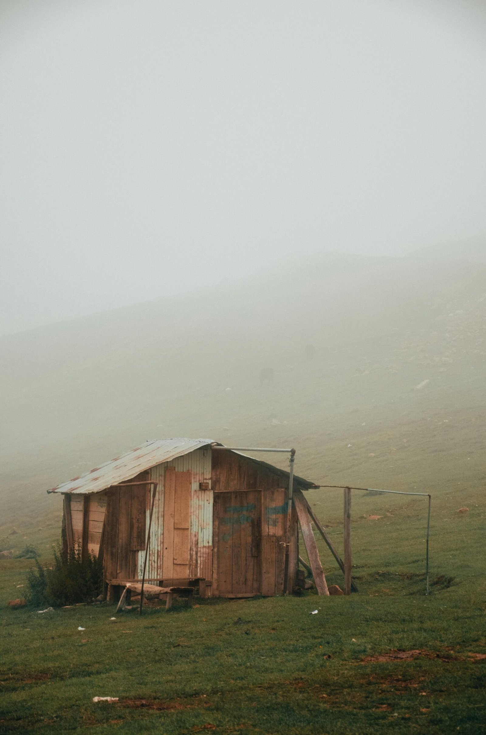 pexels-photo-3164593-3164593 A rustic wooden cabin sits isolated in a foggy rural landscape, surrounded by misty fields.